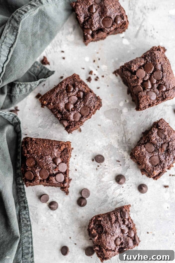 Overhead shot of 6 perfectly sliced vegan oat flour brownies arranged on a grey surface, with scattered chocolate chips, ready to be enjoyed.