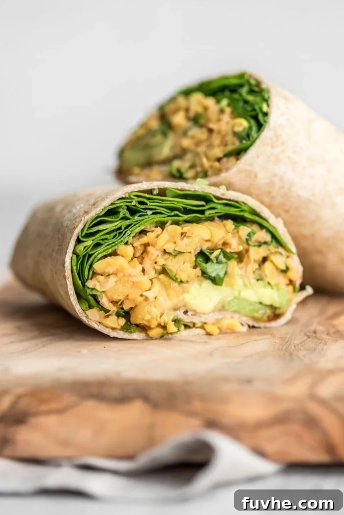 Kickin' Chickpea Avocado Wraps 6 Close-up of a spicy chickpea wrap cut in half, revealing the vibrant filling of chickpeas, spinach, and avocado, resting on a wooden cutting board.