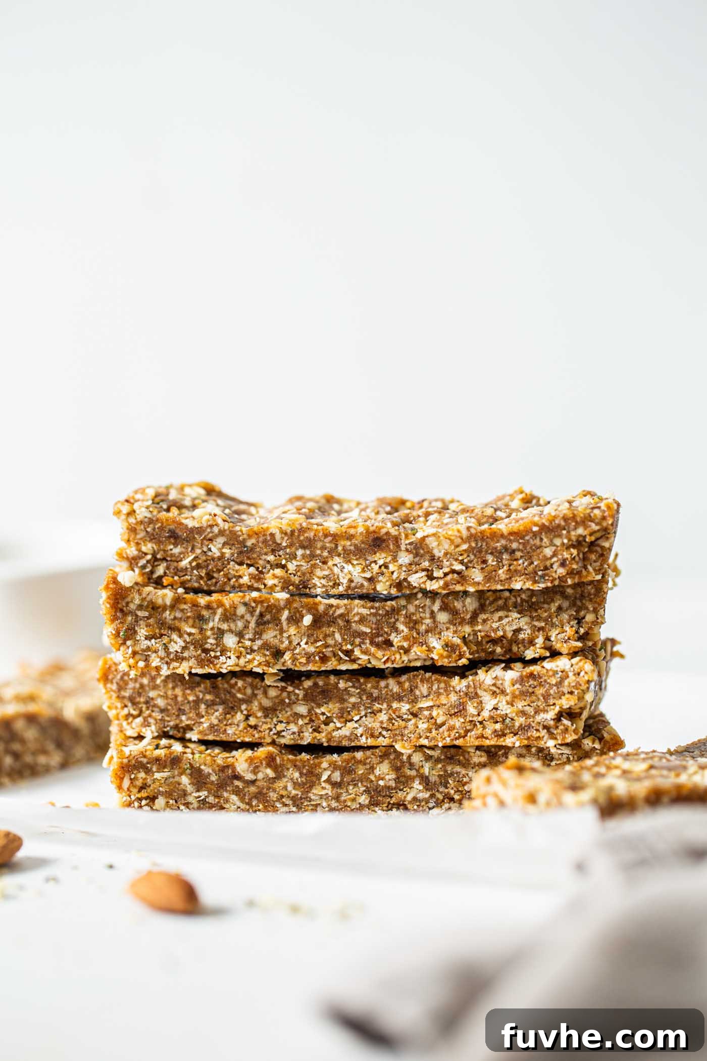 A stack of 4 no-bake oatmeal energy bars on a counter with scattered almonds, highlighting their wholesome ingredients and appealing texture.