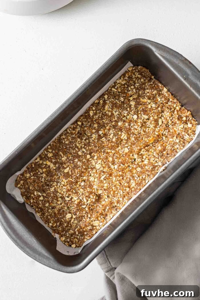 No-bake energy bar dough firmly pressed into a parchment paper-lined loaf pan, ready for chilling.