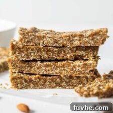 A stack of 4 energy bars on a counter with a few almonds scattered around them.