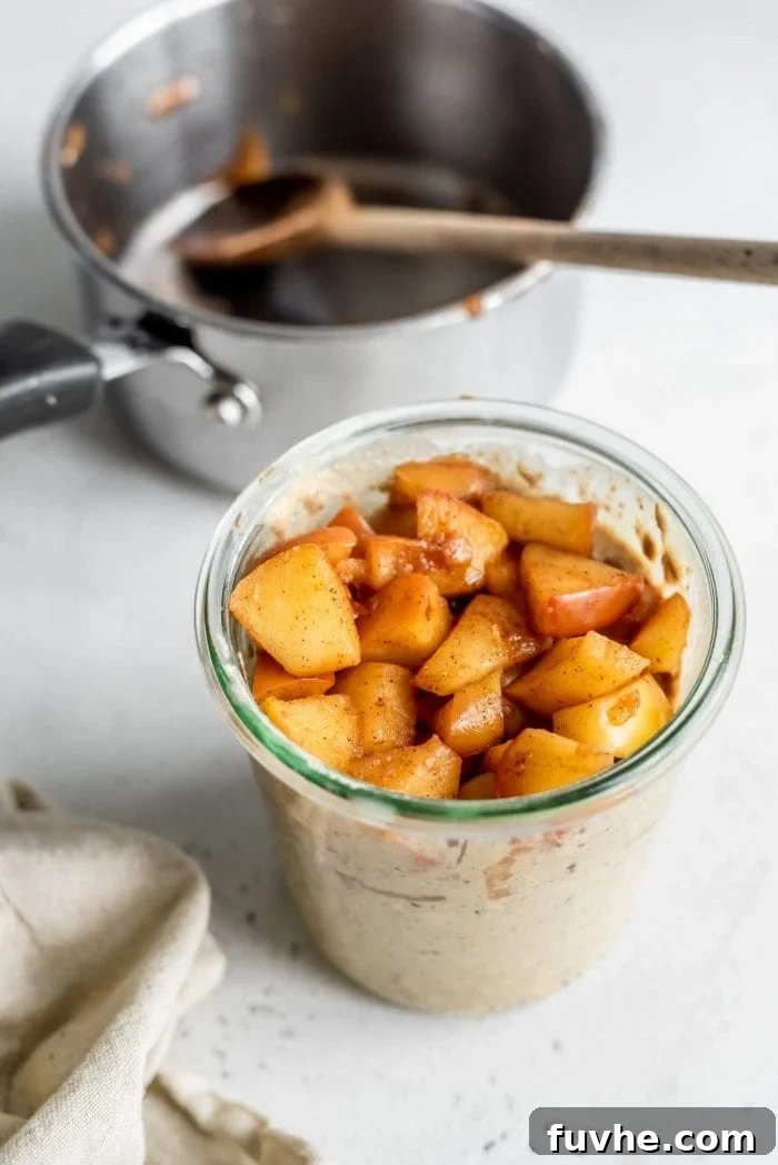 Cooked diced apples carefully layered into a jar with overnight oats, ready for chilling.
