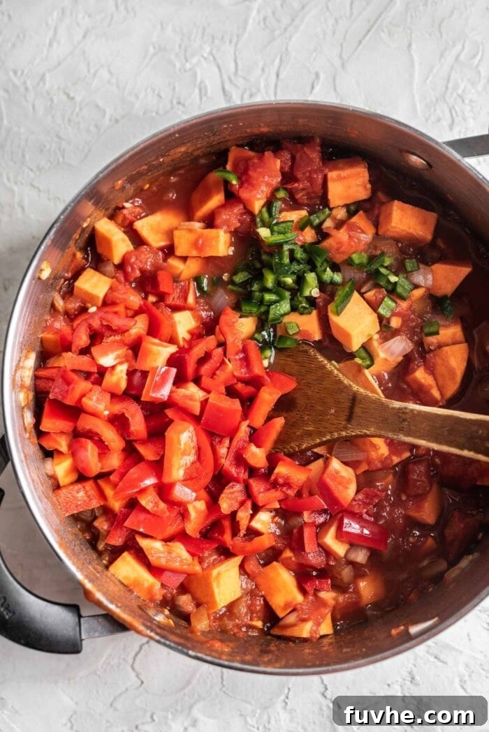 Red pepper and jalapeno being added to a large pot of chili.
