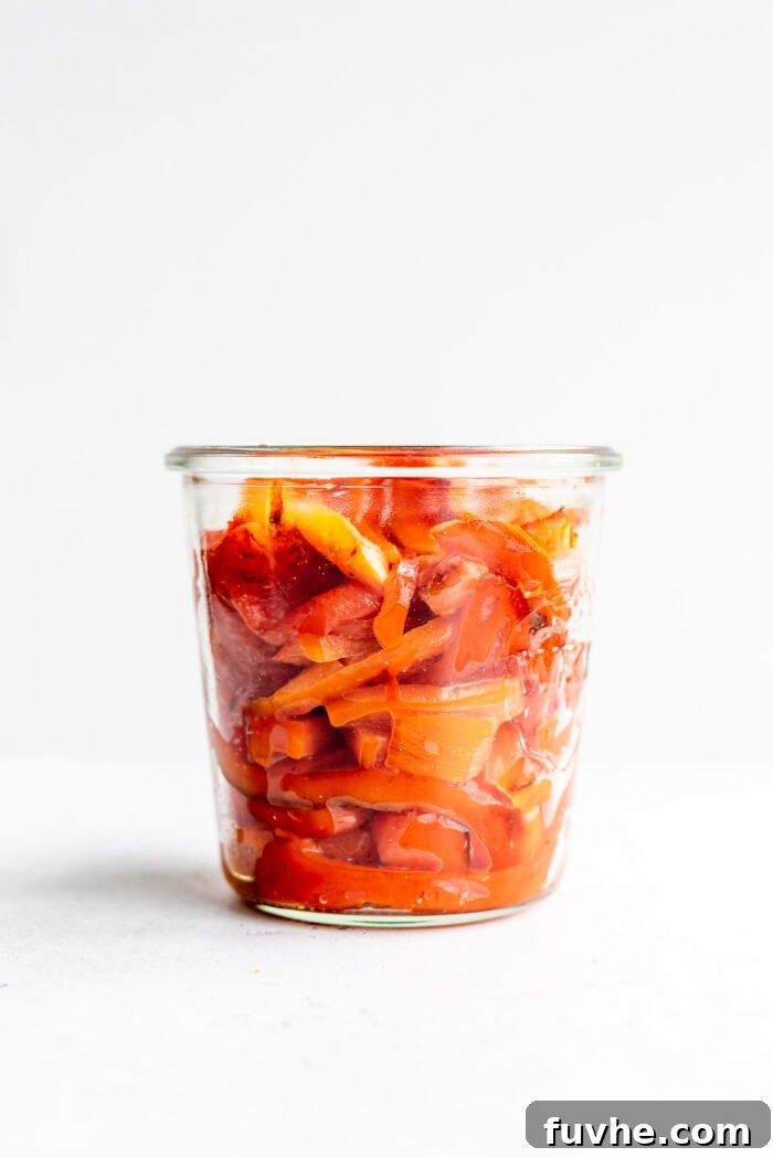Perfect Roasted Peppers 2 A glass jar filled with perfectly sliced roasted red peppers, set against a clean white background.
