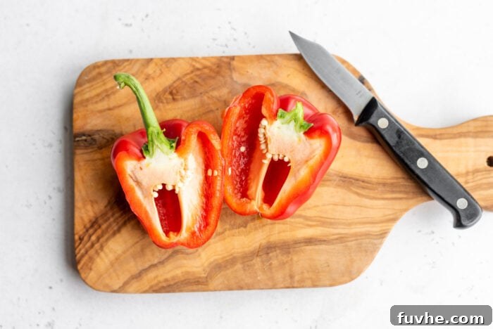 Perfect Roasted Peppers 3 A bright red bell pepper expertly cut in half on a wooden cutting board, with a chef's knife nearby.