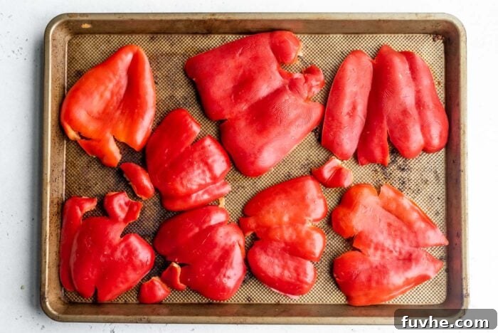 Perfect Roasted Peppers 5 Several vibrant red bell pepper halves are smashed flat on a metal baking tray, skin side up, ready for the oven.