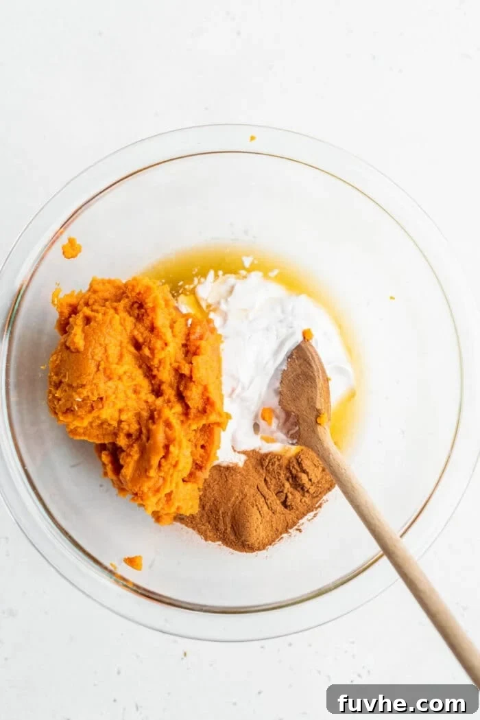 Individual ingredients including pumpkin puree, pumpkin pie spice, coconut cream, and maple syrup in a bowl before mixing.