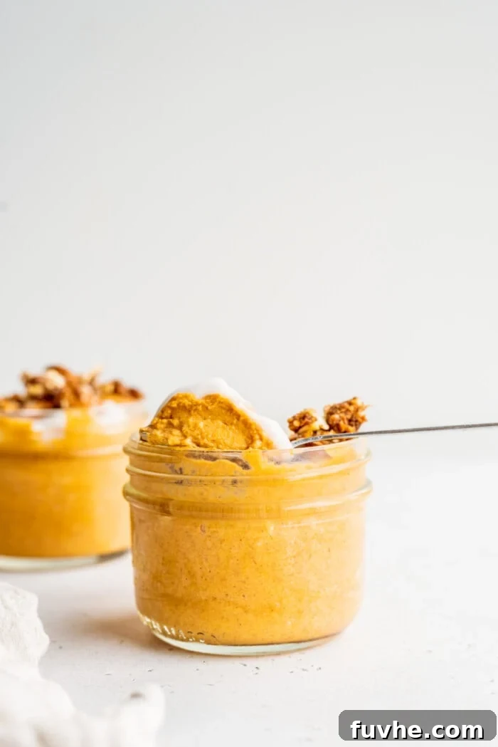 A spoon scooping a generous portion of pumpkin mousse from a jar, highlighting its creamy texture.