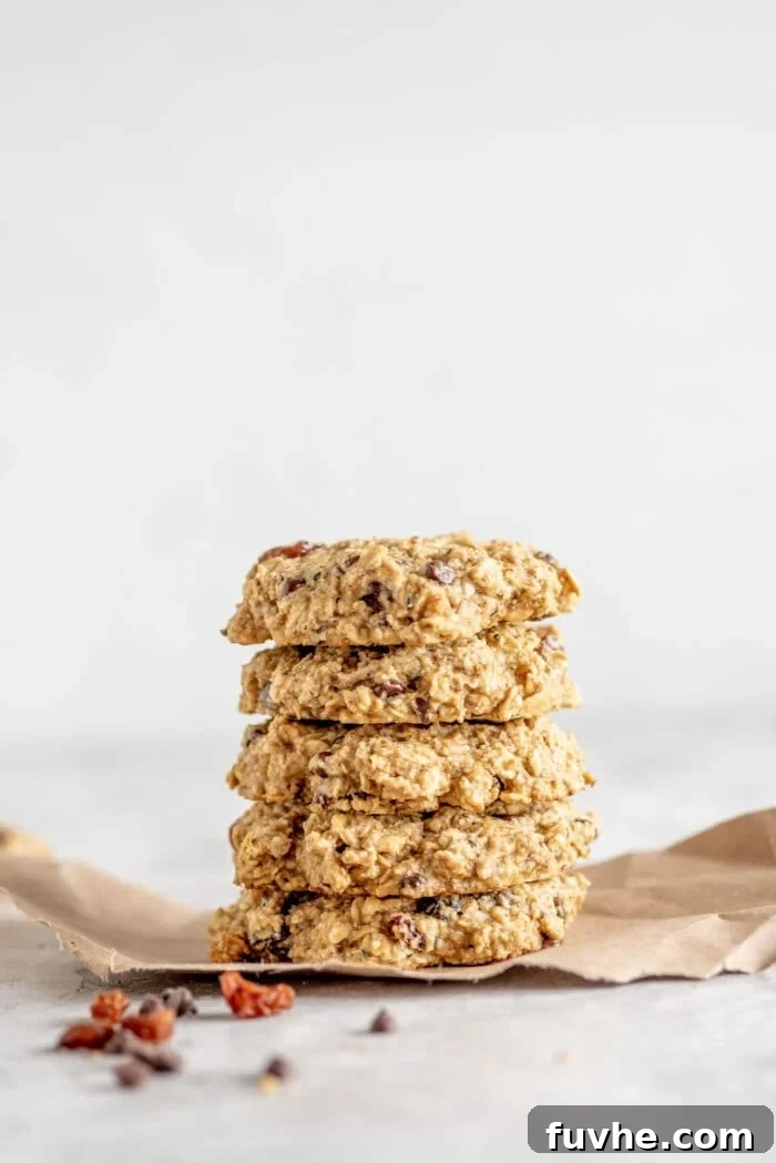 A stack of vegan and gluten-free, healthy oat cookies resting on brown paper with some raisins scattered around, highlighting their rustic charm.