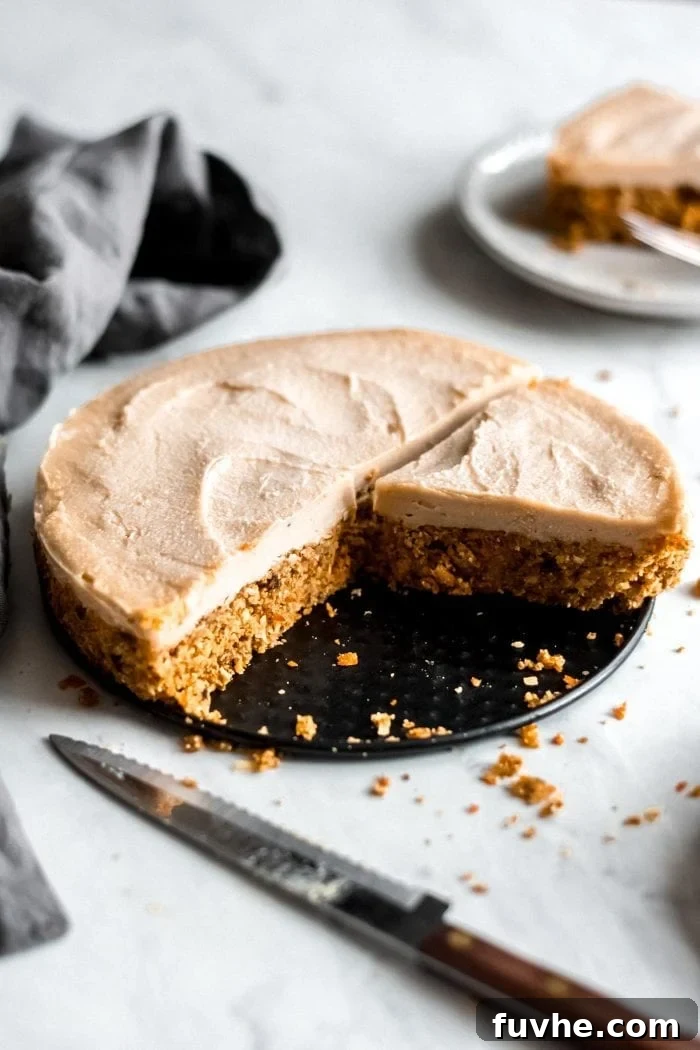 A beautiful, perfectly sliced raw vegan carrot cake rests on a springform pan, a knife nearby, showcasing its distinct layers of spiced cake and creamy white frosting.