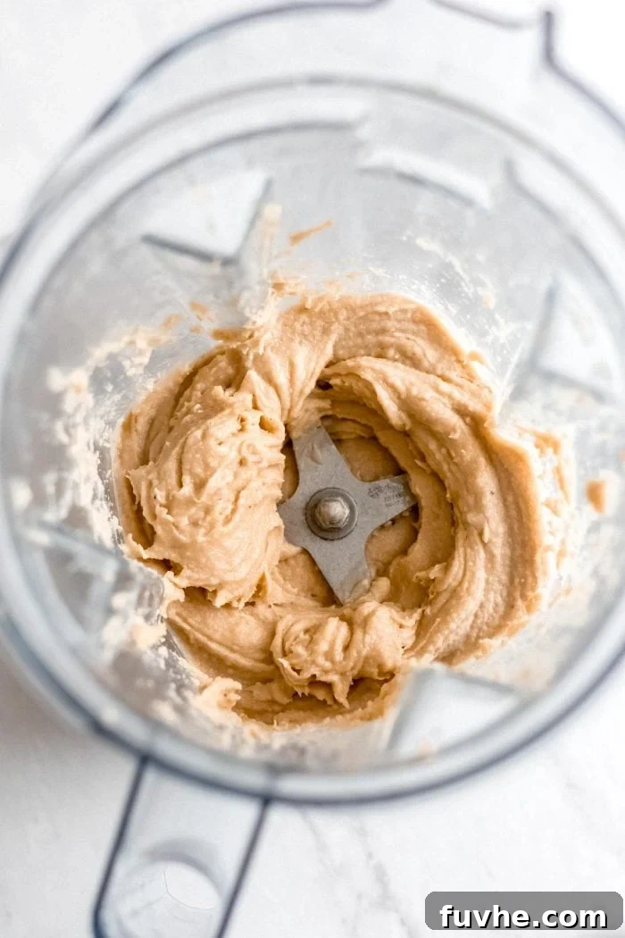 The velvety smooth cashew frosting swirling inside a blender, signaling it's perfectly prepared for topping the raw vegan carrot cake.