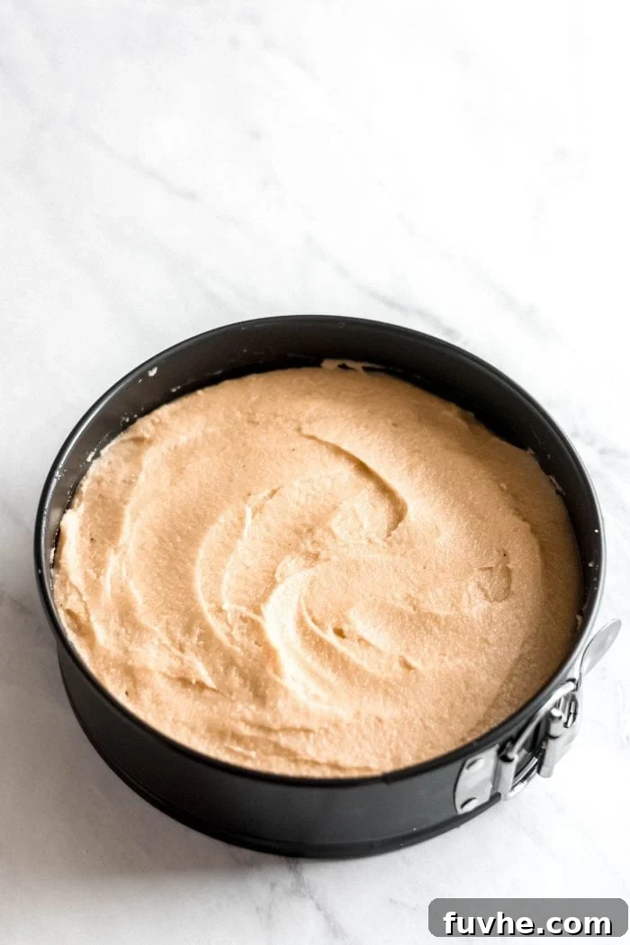 The assembled raw carrot cake, beautifully frosted and contained within a springform pan, sits prepared and ready for chilling in the freezer.