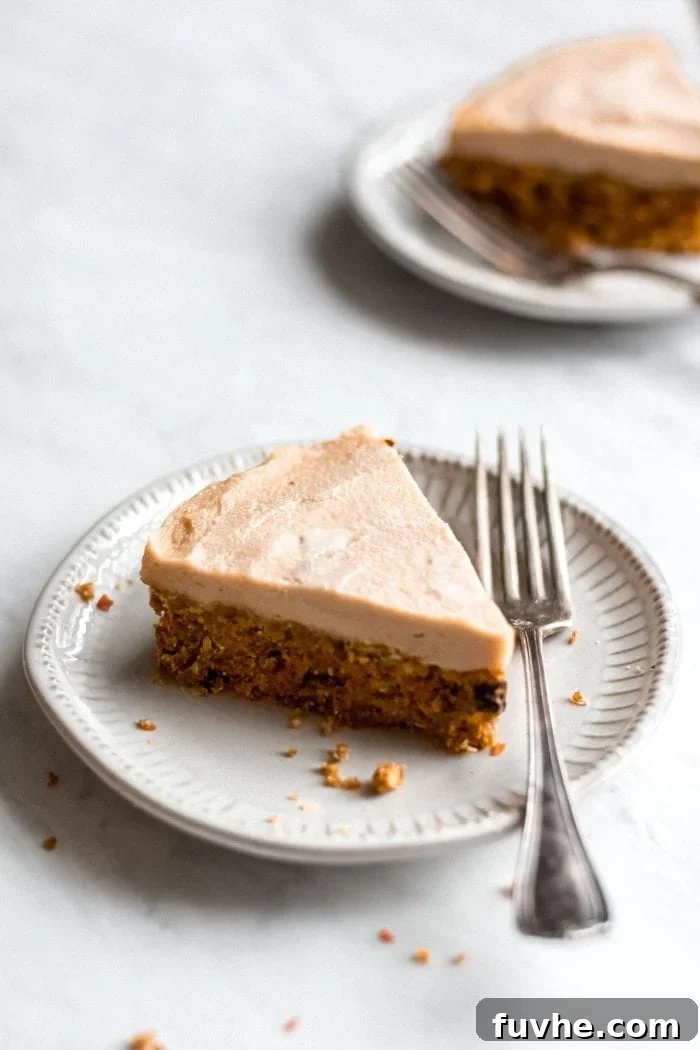 A large, inviting slice of raw vegan carrot cake with a thick layer of cashew frosting, presented elegantly on a white plate with a fork, ready to be savored.
