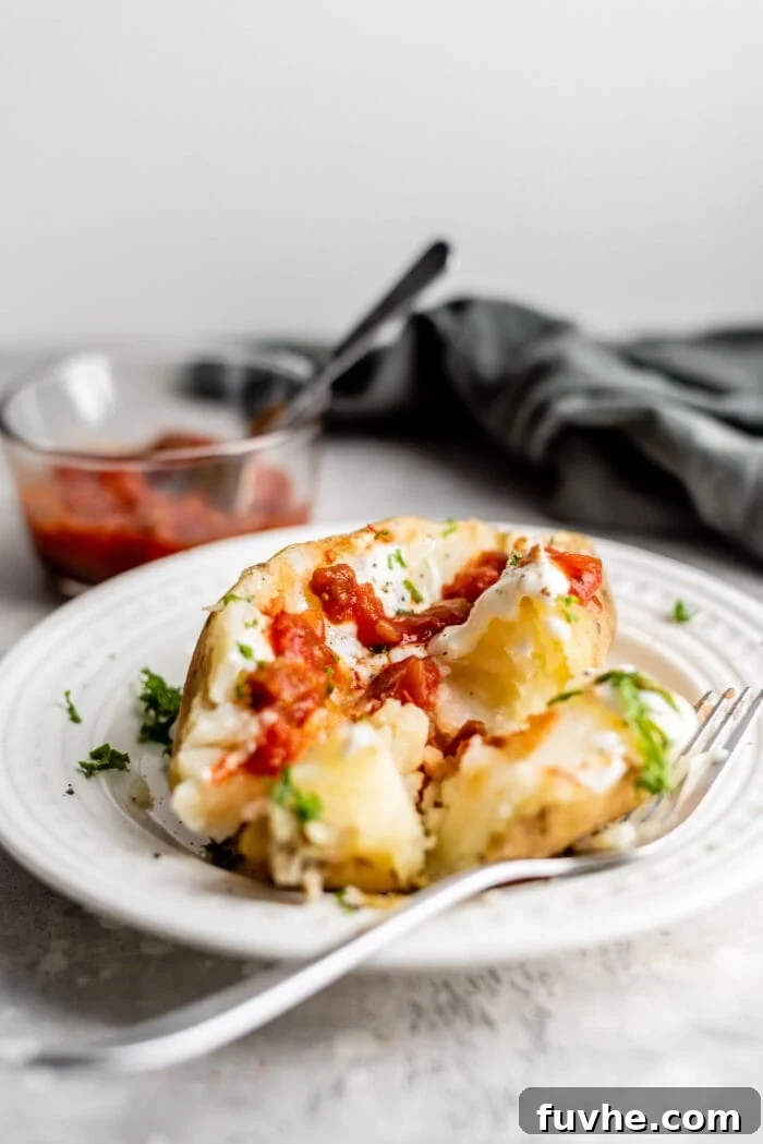 Perfect Instant Pot Baked Potatoes 9 A baked potato with sour cream, parsley and salsa on a small white plate.