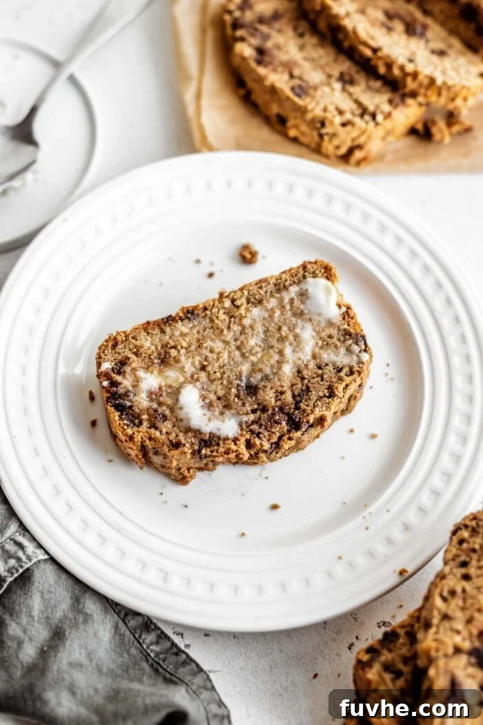 Decadent Vegan Chocolate Chip Banana Loaf 13 A single slice of moist vegan chocolate chip banana bread, generously slathered with creamy vegan butter, ready to be enjoyed.