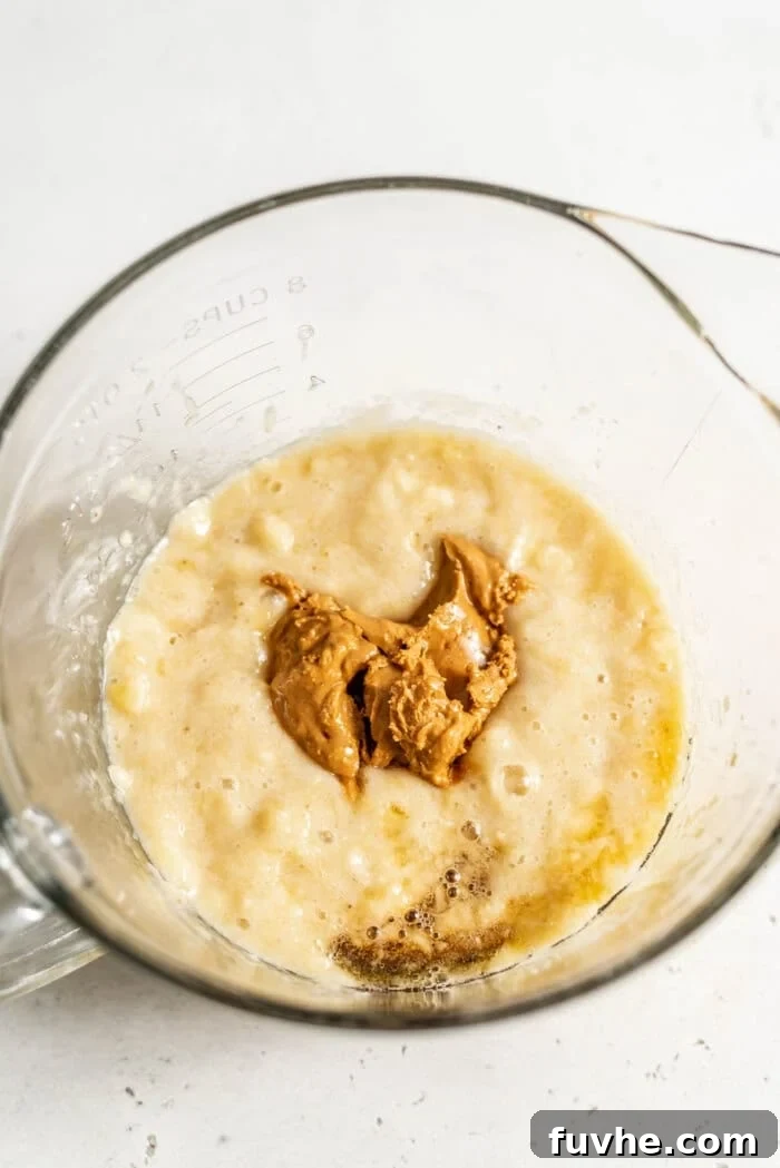 Decadent Vegan Chocolate Chip Banana Loaf 5 Three core wet ingredients – mashed banana, creamy nut butter, and golden maple syrup – mixed in a glass bowl.