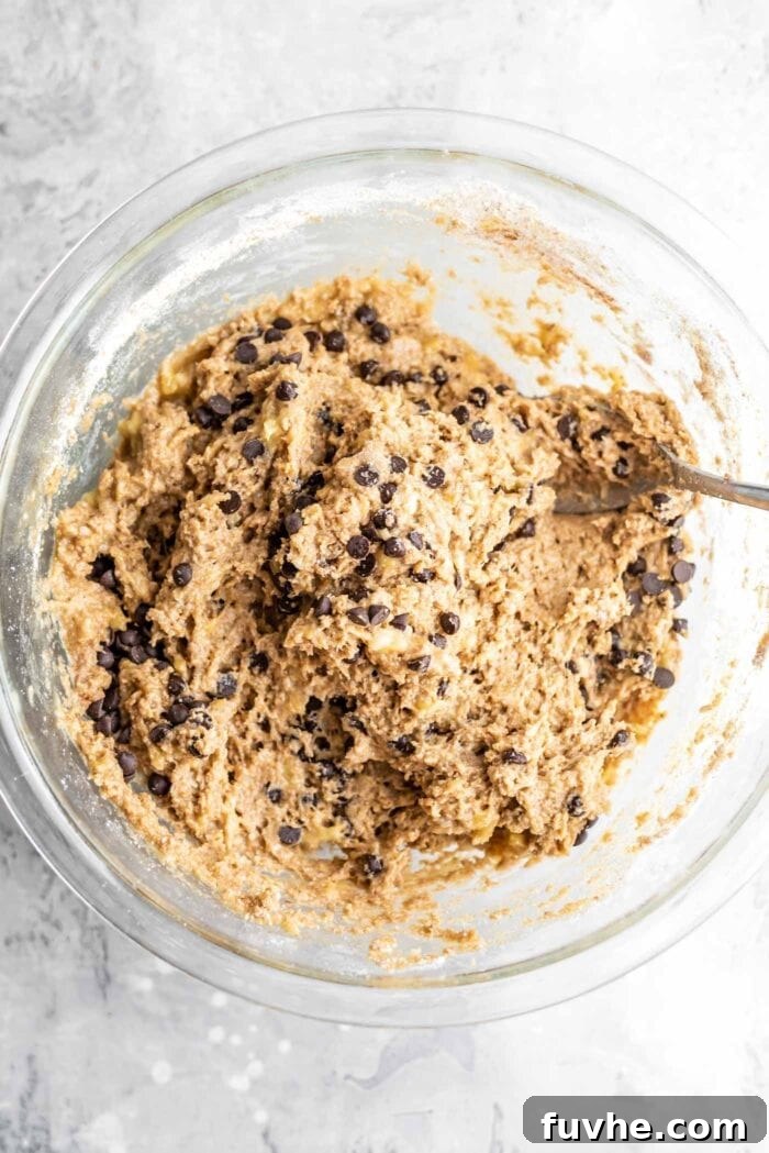 Decadent Vegan Chocolate Chip Banana Loaf 9 A smooth, raw banana bread batter, studded with dairy-free chocolate chips, resting in a glass mixing bowl, ready for baking.