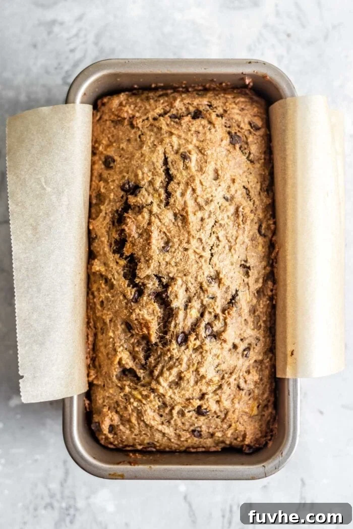 Decadent Vegan Chocolate Chip Banana Loaf 10 A perfectly baked loaf of vegan banana bread, fresh from the oven, still in its parchment-lined loaf pan.