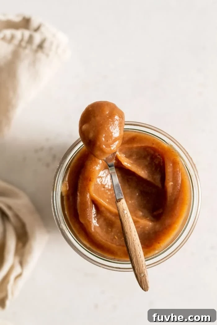 A spoon scooping apple butter out of a glass jar.