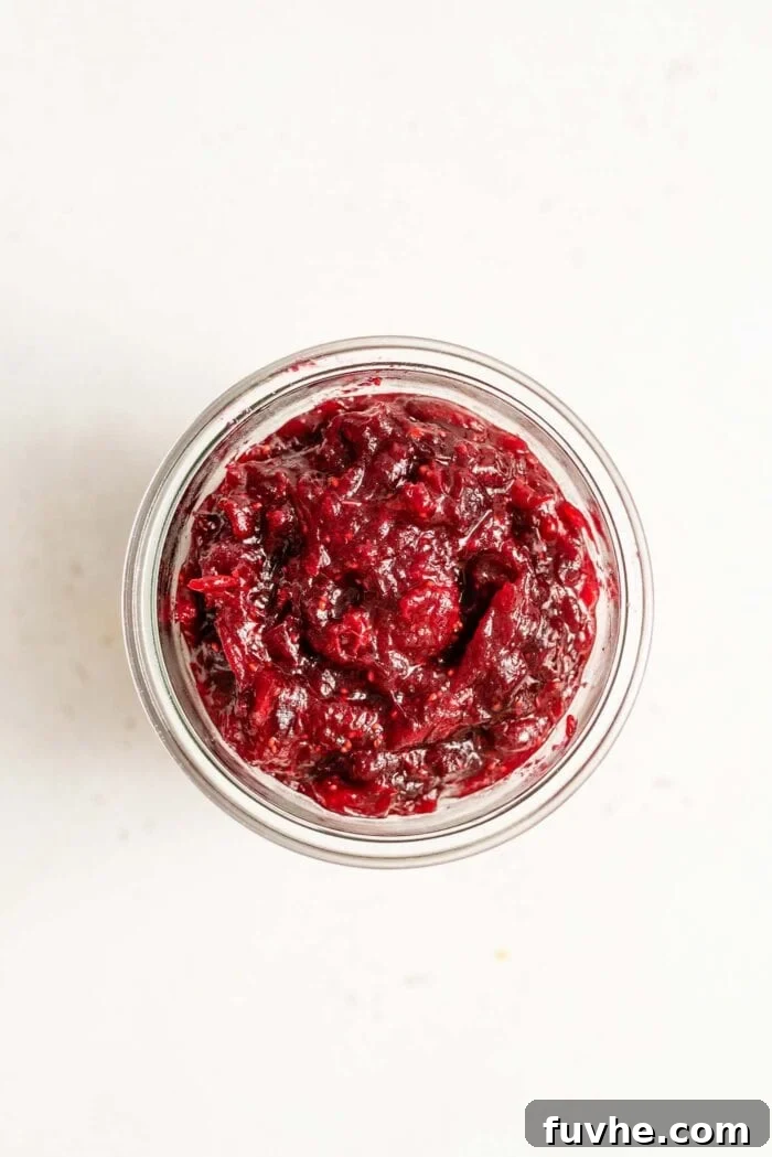 Artisan Cranberry Preserve 6 Overhead image of a glass jar filled with homemade cranberry sauce sitting on a white surface, ready to be served or stored.