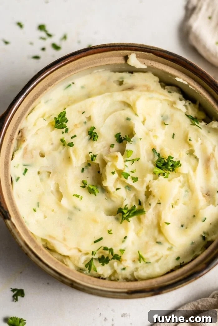 A serving dish full of vegan mashed potatoes topped with fresh parsley.