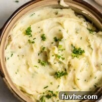 A serving dish full of vegan mashed potatoes topped with fresh parsley.
