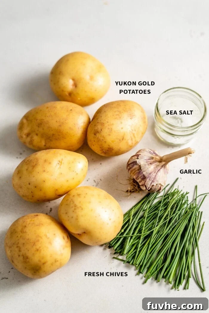6 Yukon Gold potatoes, sea salt, fresh chives and a bulb of garlic sitting on a white surface.