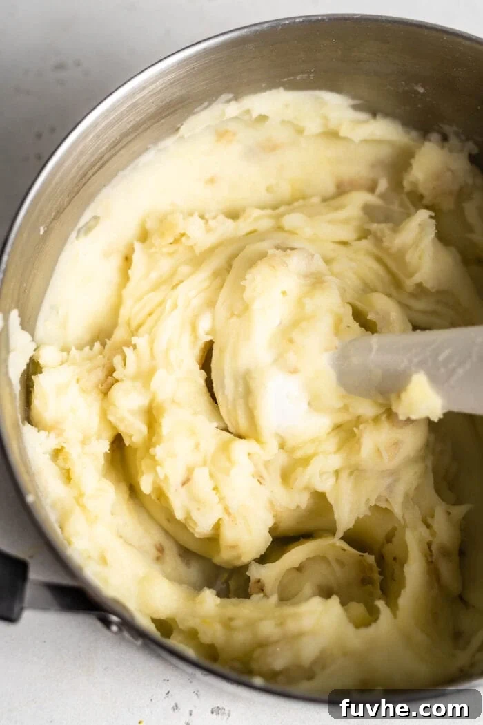 An immersion blender mixing mashed potatoes in a large pot.