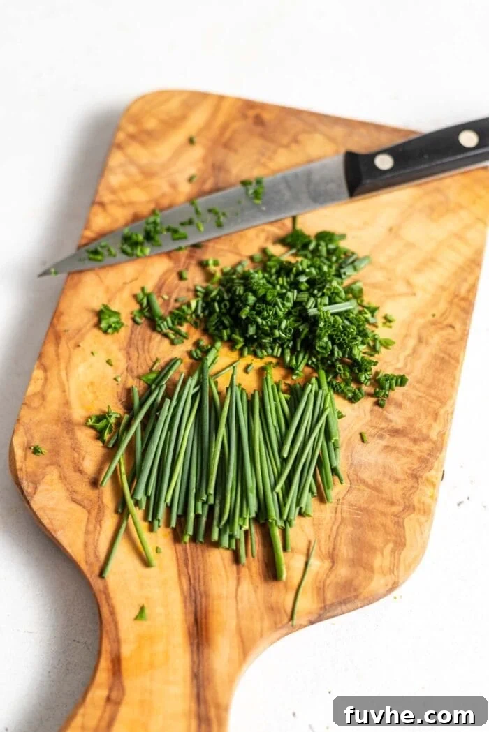 Chopped chives and a knife on a cutting board.