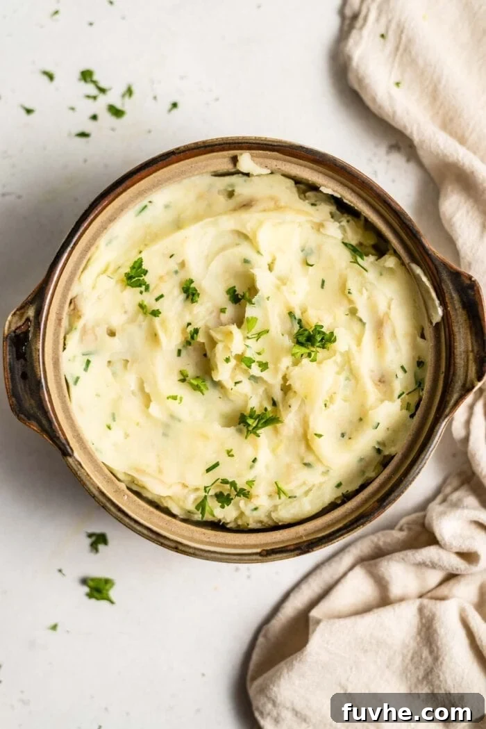 A serving dish full of vegan mashed potatoes topped with fresh chopped parsley and chives.