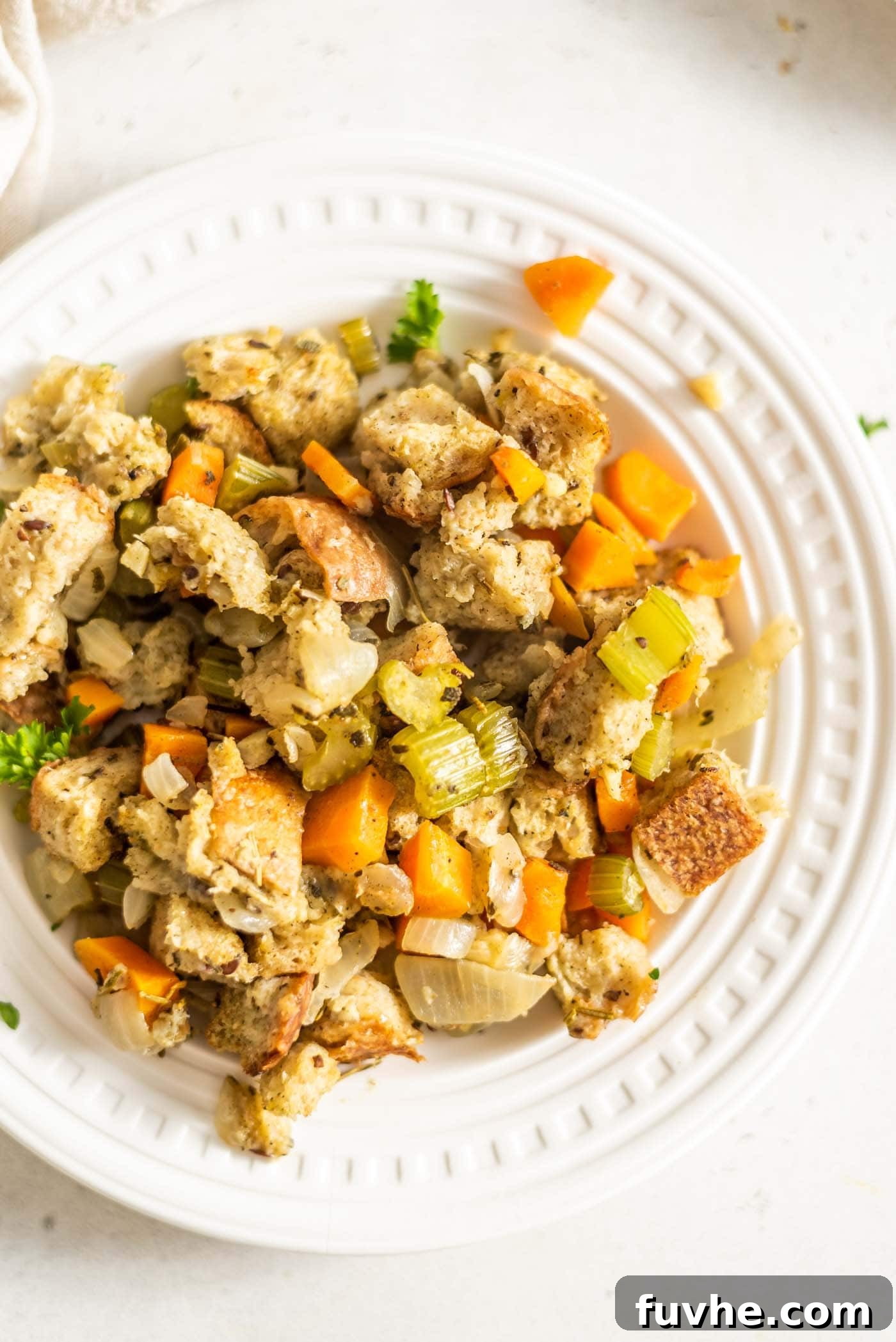 A small plate showcasing perfectly baked, golden-brown plant-based stuffing made with cubed bread and finely diced vegetables, garnished with fresh herbs.
