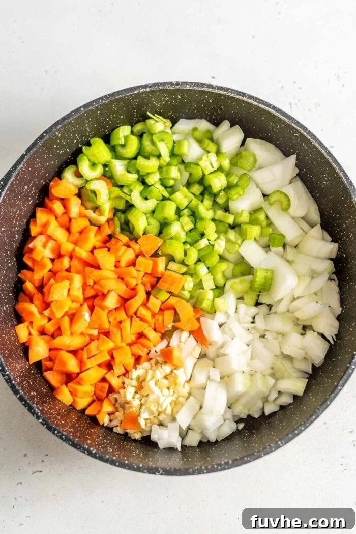 A vibrant mix of finely diced carrots, onions, celery, and minced garlic gently sautéing in a large skillet, creating an aromatic base for the stuffing.