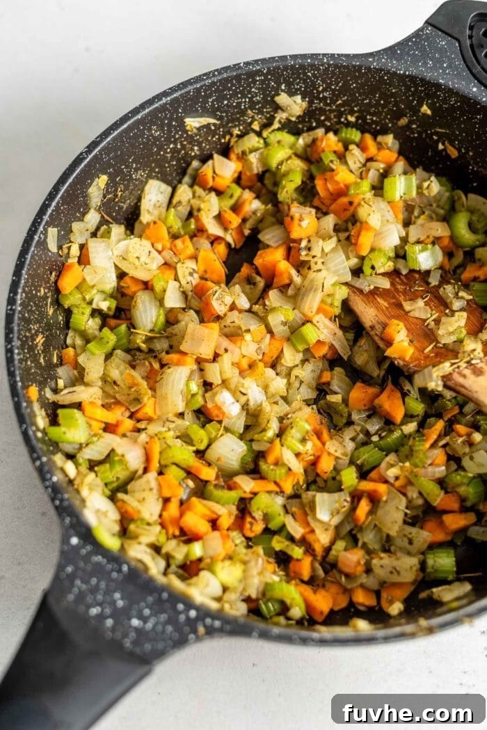 A close-up shot of sautéed garlic, onion, celery, and carrot mixture in a skillet, now infused with fragrant herbs, ready for the next step of the stuffing preparation.