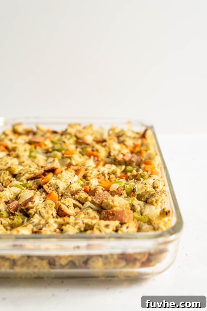 A large casserole dish brimming with vegan stuffing, featuring a rich blend of bread and colorful vegetables, baked to a perfect golden-brown on top, fresh out of the oven.