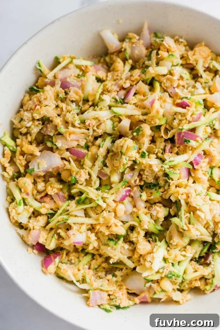 Raw chickpea burger batter with zucchini and red onion in a large mixing bowl.