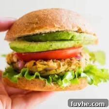 Hand holding a chickpea veggie burger on a bun with lettuce, tomato, onion and avocado.