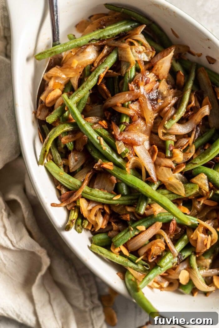 Garlicky Onion Green Bean Sauté 2 Sauteed green beans with onions, garlic and slivered almonds in a serving dish with a spoon.