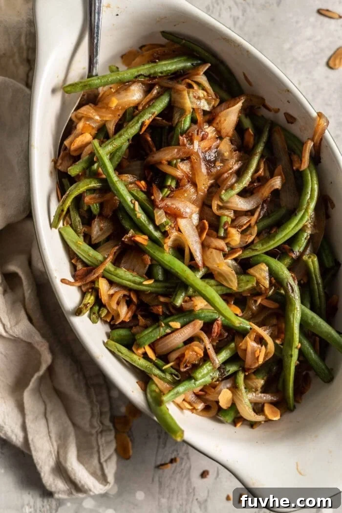 Garlicky Onion Green Bean Sauté 8 Sauteed green beans with onions, garlic and slivered almonds in a serving dish with a spoon.
