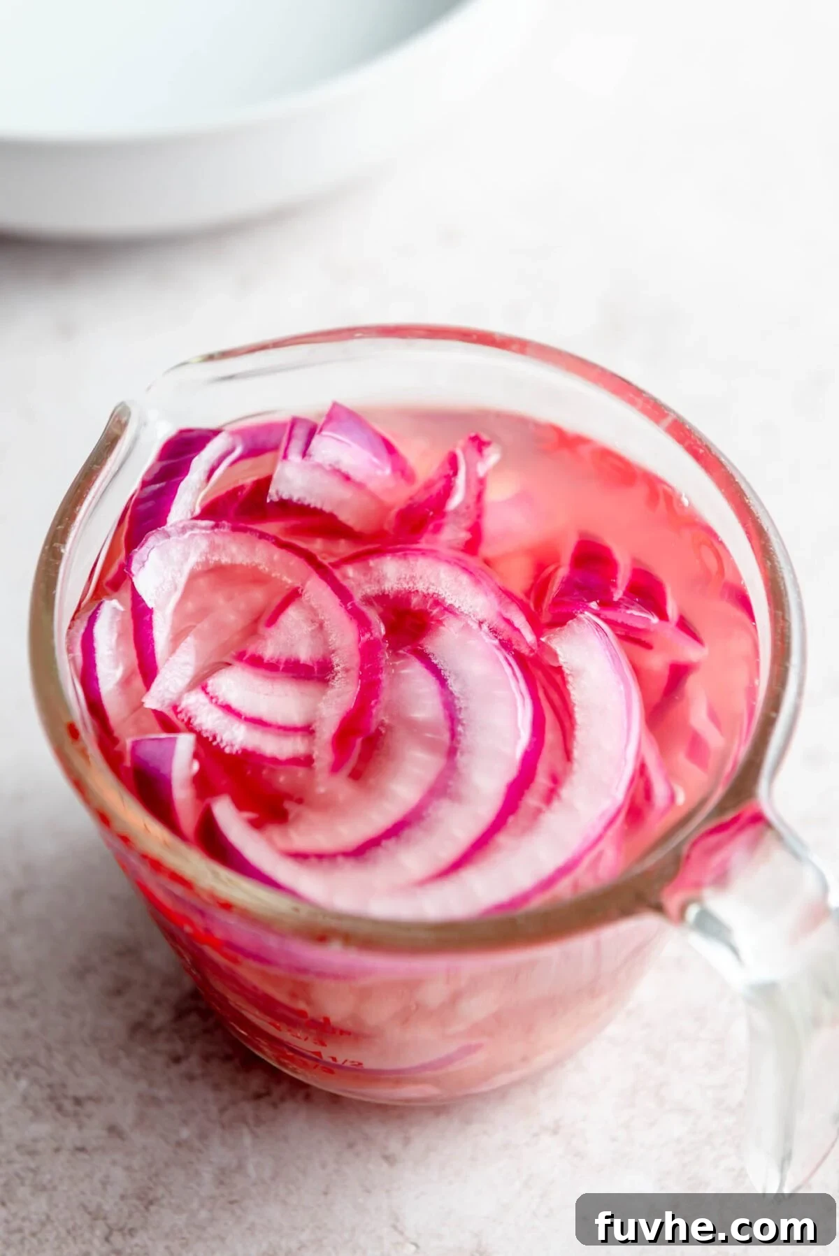 Thinly sliced red onions pickling in a glass container with vinegar and hot water.