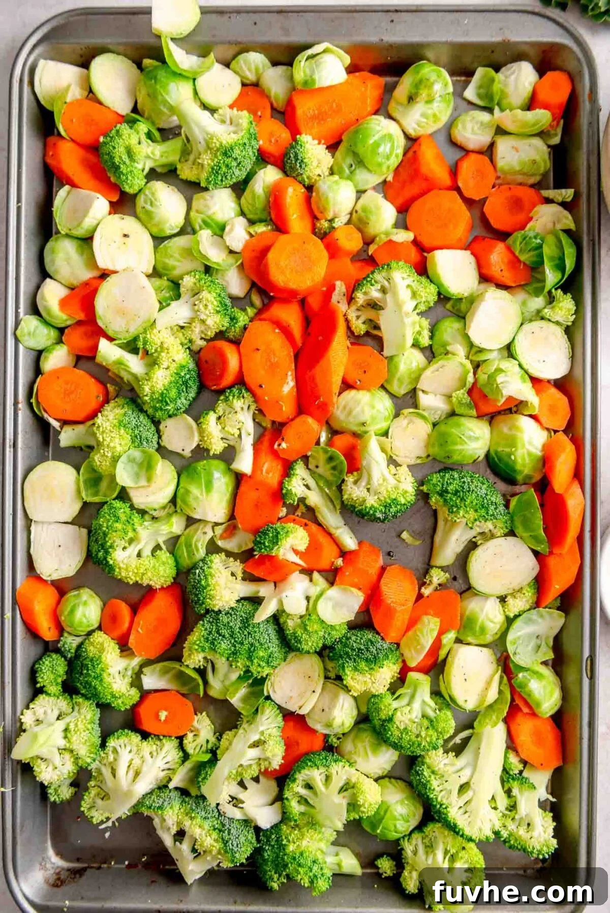 Chopped Brussels sprouts, carrots, and broccoli spread on a large baking sheet for roasting.