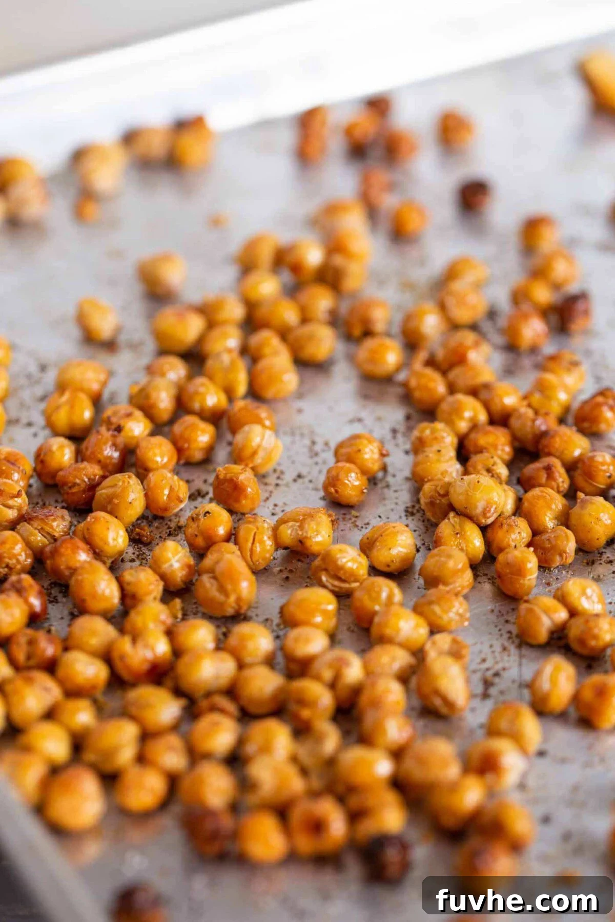 Seasoned chickpeas spread on a baking tray, ready for roasting.