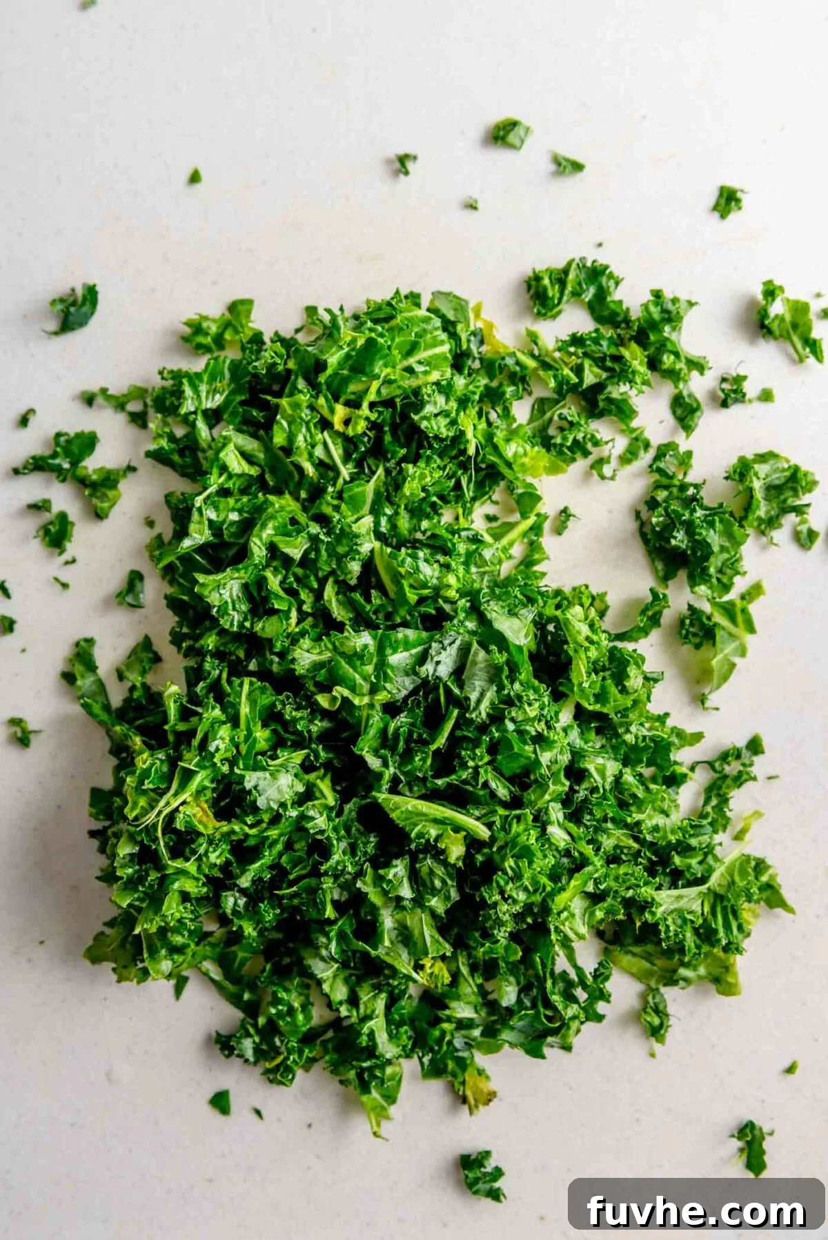 Finely chopped kale being massaged with oil on a cutting board.