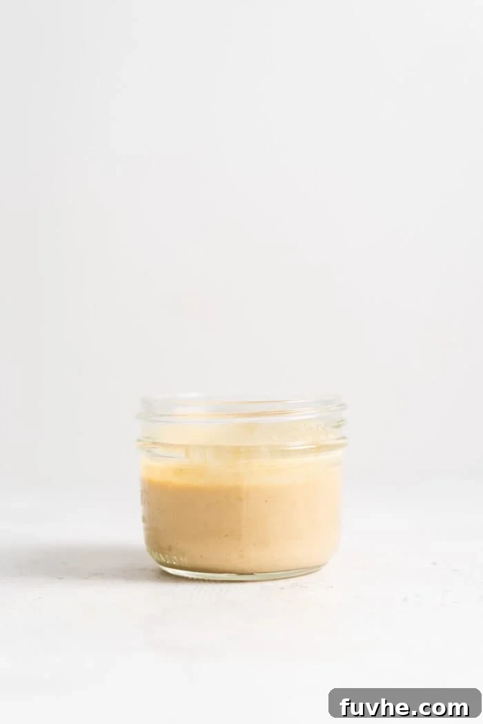 A close-up of creamy miso tahini dressing in a small glass jar, garnished with a sprinkle of sesame seeds, highlighting its rich texture.