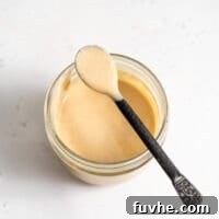 A spoon scooping creamy miso tahini dressing out of a small glass jar, highlighting its perfect, smooth texture.