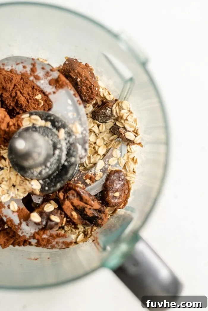 Dates, oats, and cocoa powder inside a food processor, ready to be blended into cookie dough.