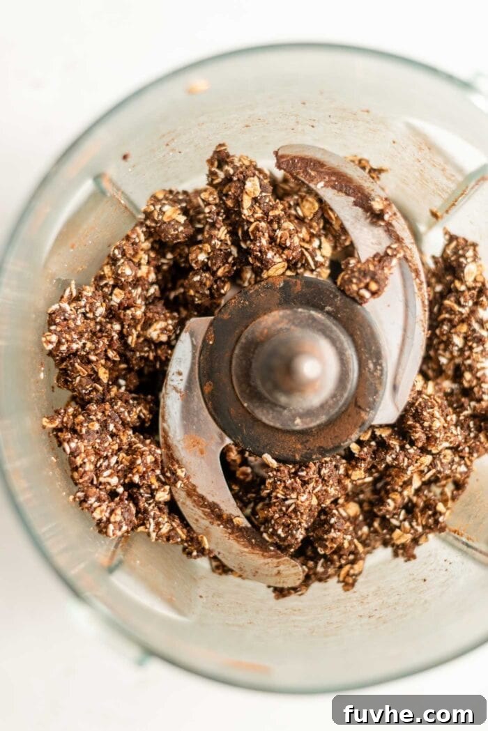 Vegan raw chocolate cookie dough in a food processor, after being pulsed into a crumbly mixture.