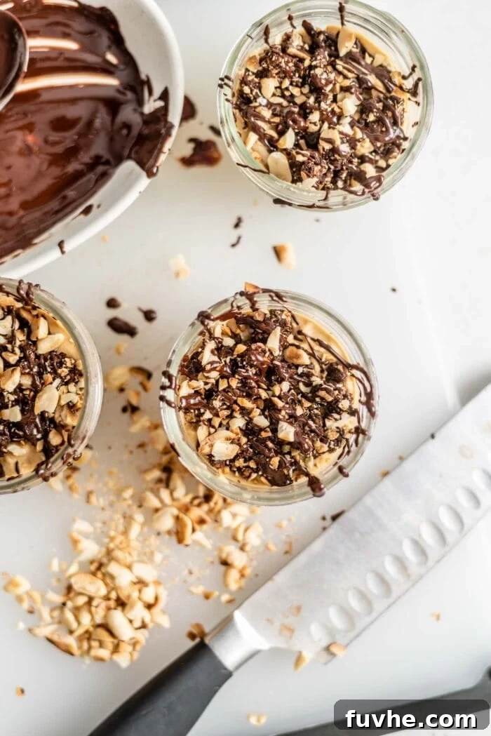 Three beautifully presented peanut butter mousse parfaits, garnished with chopped peanuts and a delicate chocolate drizzle, resting on a rustic cutting board.