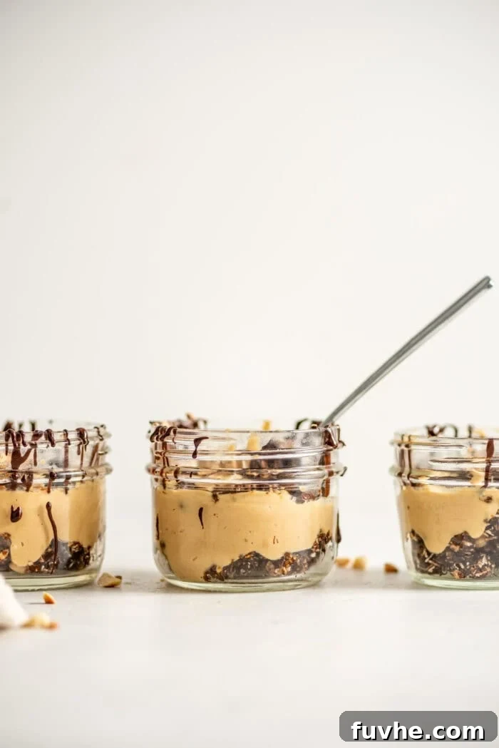 A close-up view of three peanut butter mousse parfaits in small glass jars, with a spoon gently scooping out a portion of the mousse, highlighting its creamy texture.