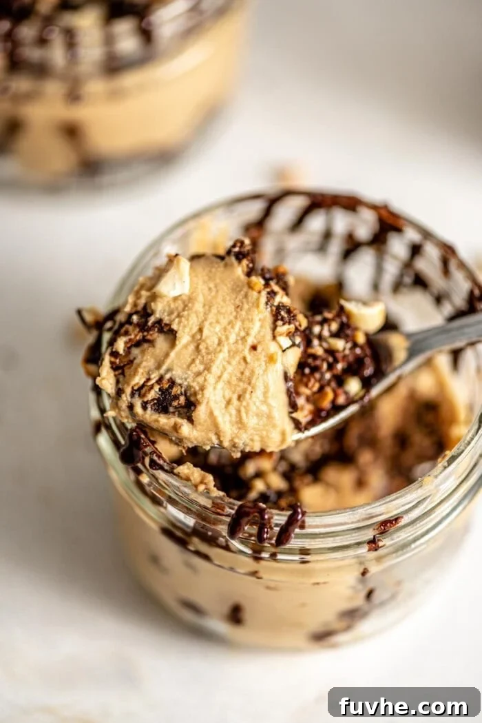 A close-up shot of a spoonful of creamy vegan peanut butter mousse, beautifully garnished with chopped peanuts and a touch of chocolate, emphasizing its smooth and appealing texture.