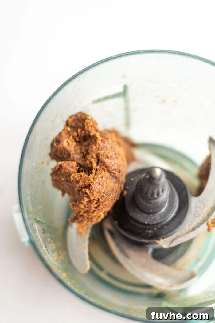 Blended dates in a food processor, forming a thick, doughy ball ready for rolling.